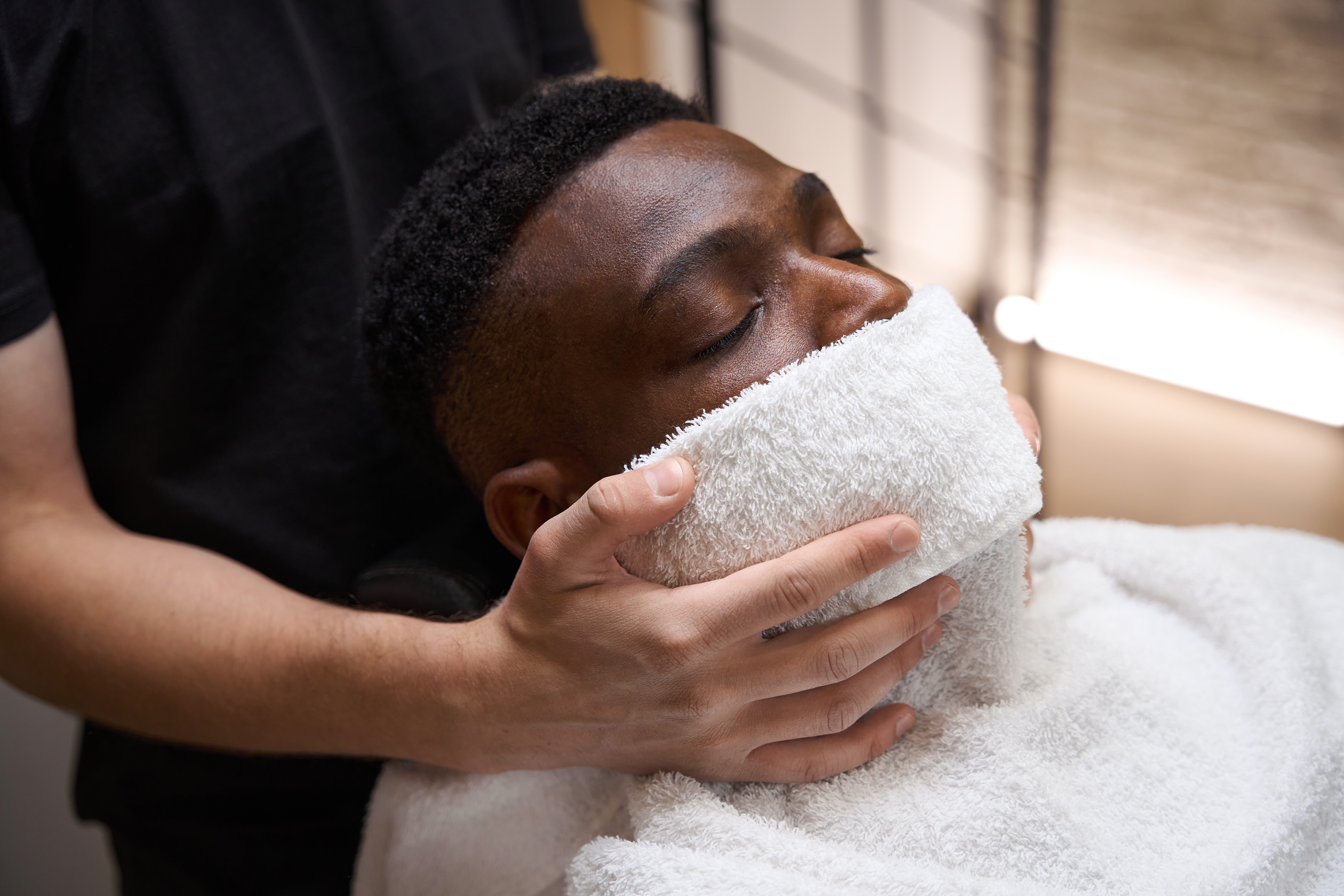 Barber put warm towel on face of African American guy