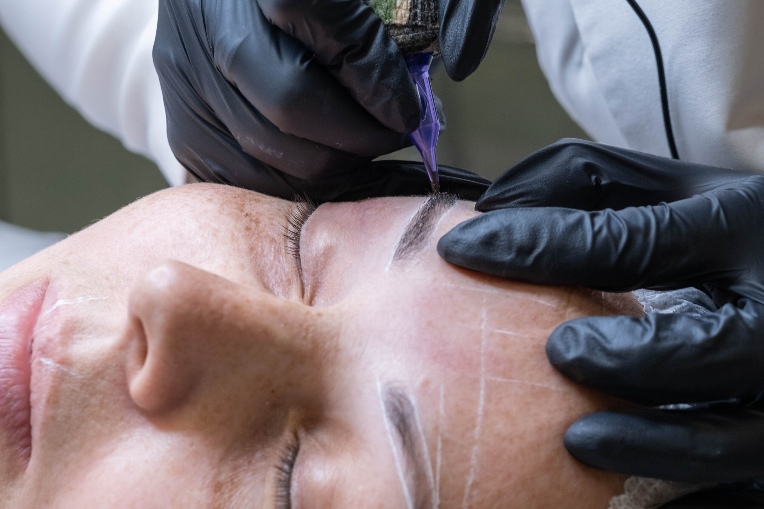 Close-up of microblading process: art of eyebrow tattooing. With gloved hands, skilled practitioner wields aspecialized needle, embedding pigment into skin. eyebrows are meticulously tinted using