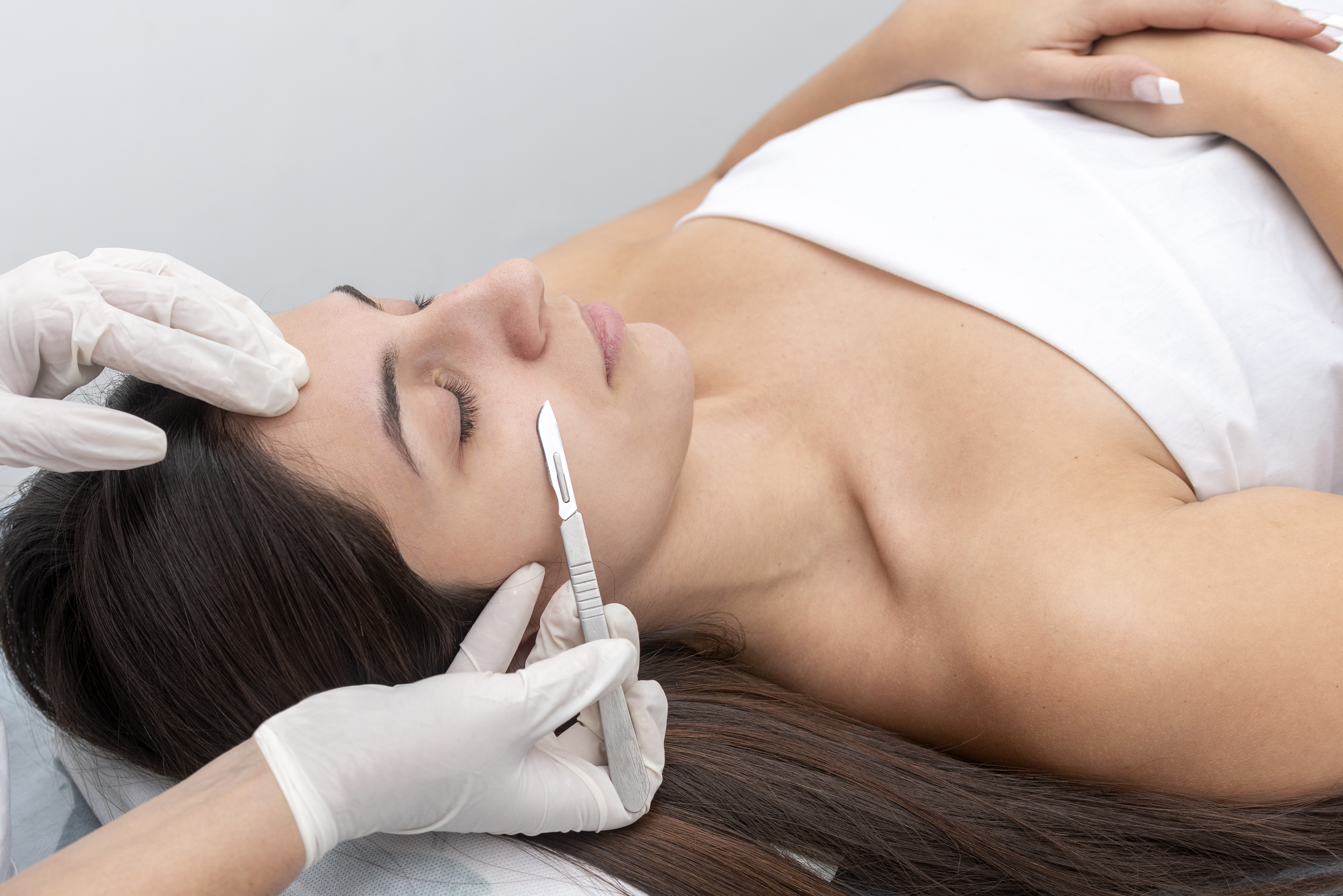 Closeup of the doctor with a scalpel treating the woman’s skin. Dermaplaning treatment.